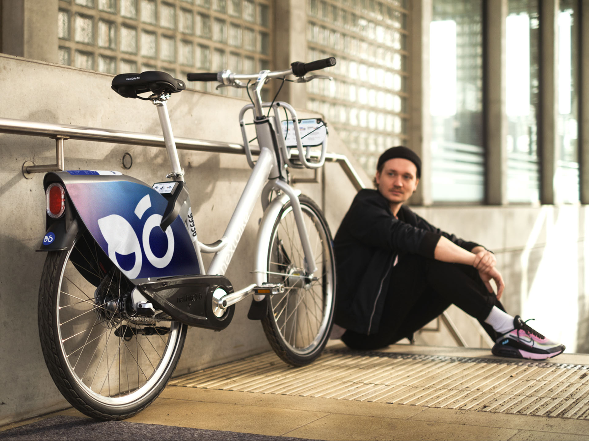 Ein junger Mann sitzt auf der oberen Stufe einer Treppe, neben ihm ein nextbike Leihrad