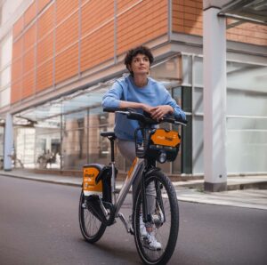campusbike-bielefeld-05-26 Eine Frau stützt sich auf dem Lenker ihres meinSiggi Leihrads ab und schaut in die Ferne