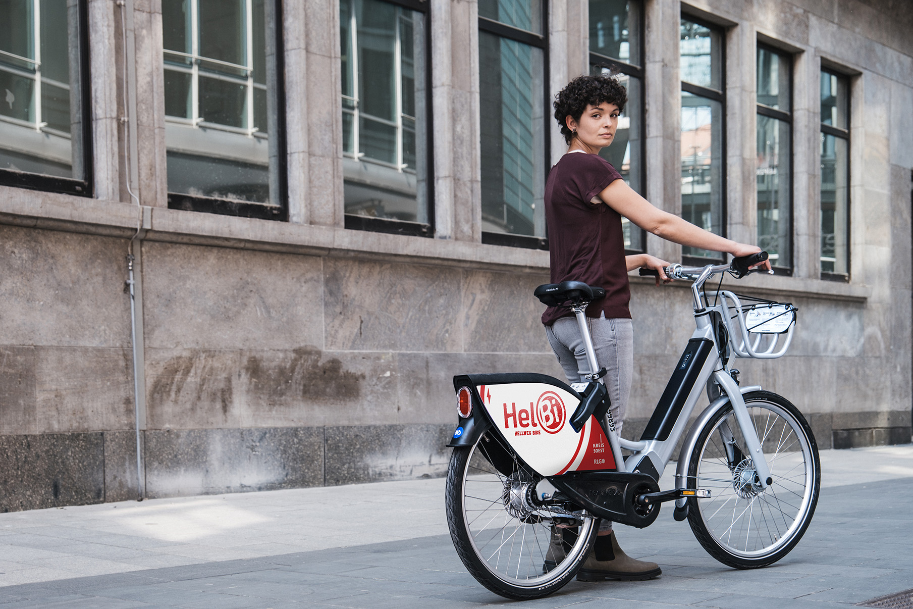 young women standing next to a HelBi bike sharing bike, slightly looking back into the camera