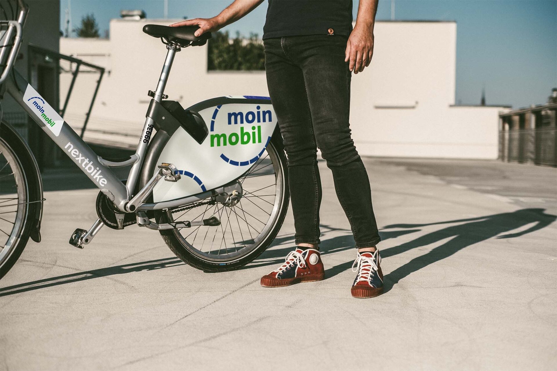 Ein Mann, den man nur von der Hüfte abwärts sieht, steht neben seinem moin mobil Leihrad.